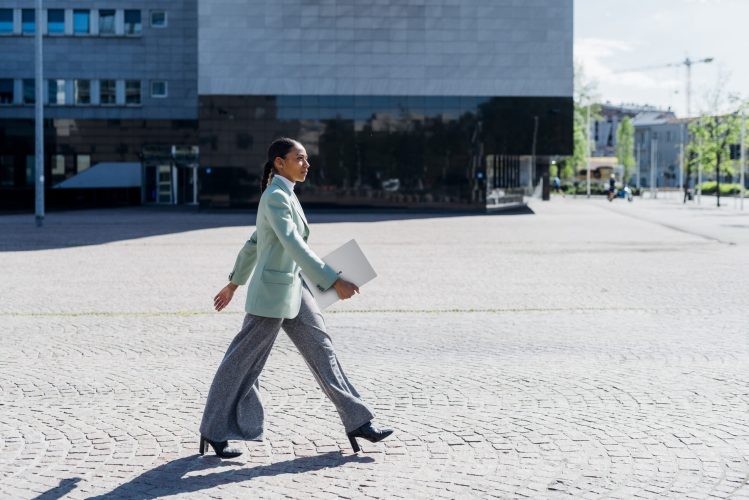 Confident businesswoman with laptop walking by office building